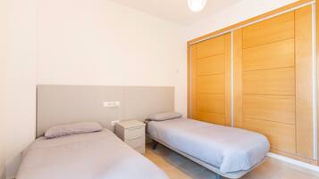 Een slaapkamer met twee eenpersoonsbedden, een nachtkastje, een houten garderobe en een lamp.