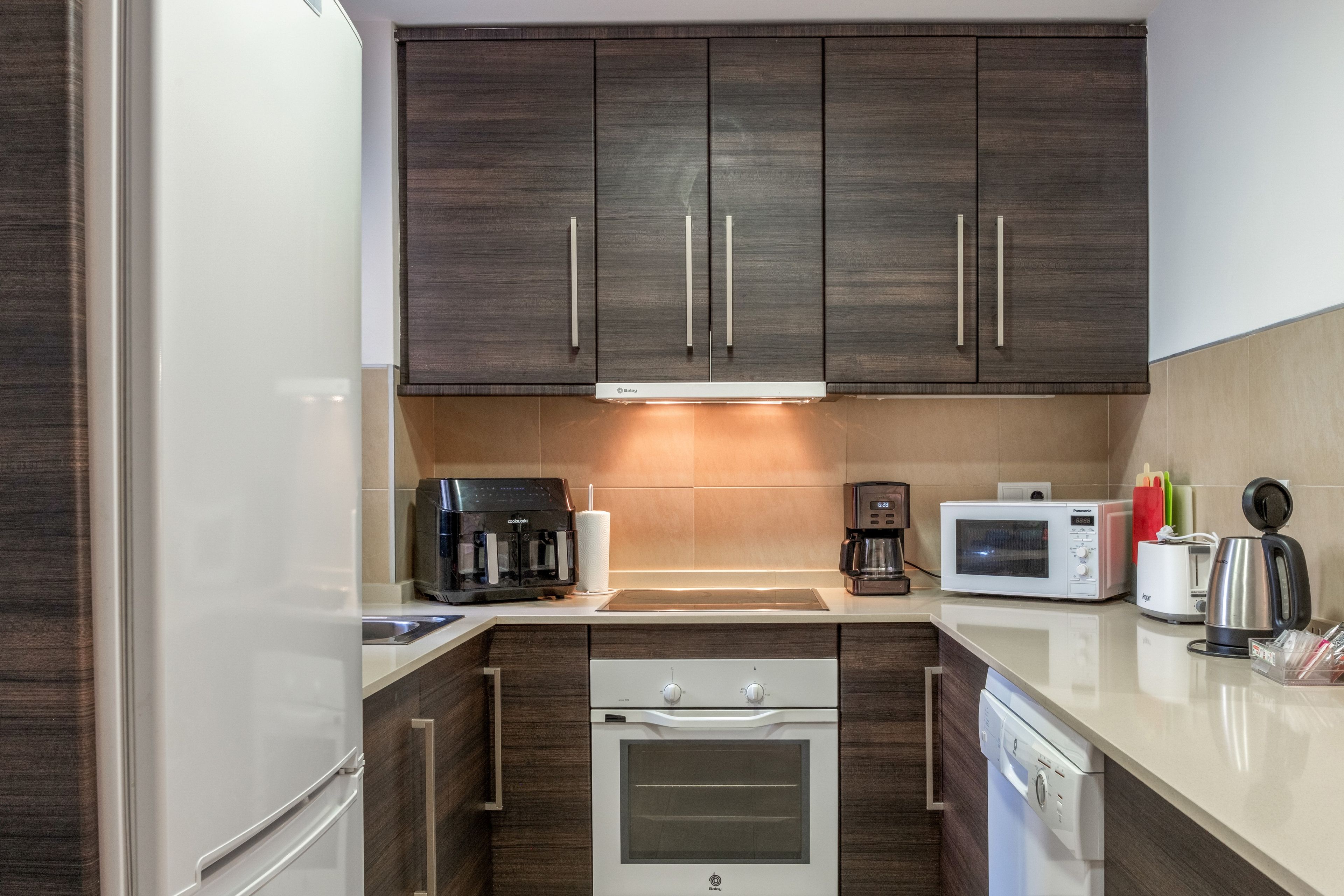 A compact kitchen with dark wood cabinets, a built-in oven, a microwave, a coffee maker, and a toaster.