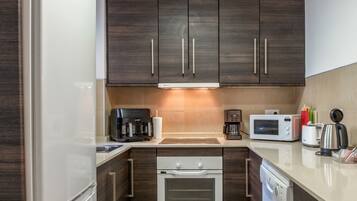 A compact kitchen with dark wood cabinets, a built-in oven, a microwave, a coffee maker, and a toaster.