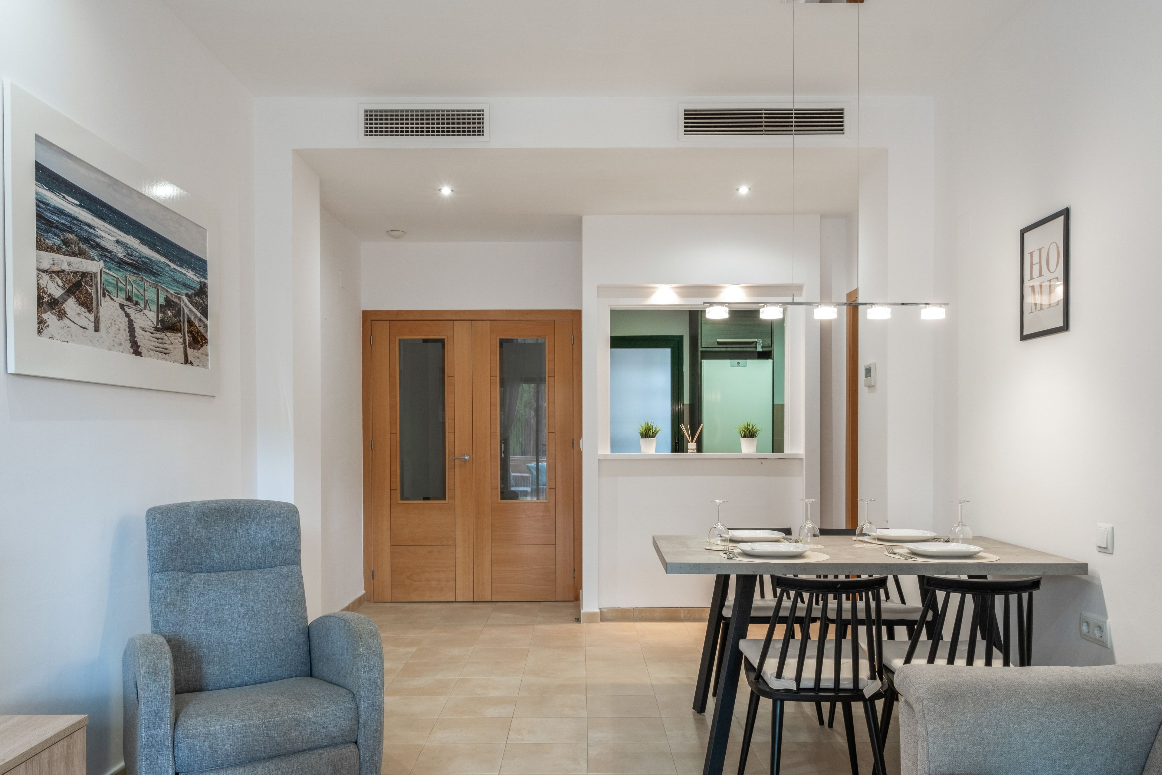 A modern dining area with a table set for four, a grey armchair, and a wooden door with glass panels.