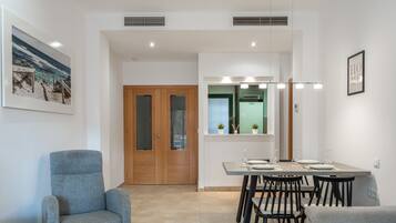 A modern dining area with a table set for four, a grey armchair, and a wooden door with glass panels.