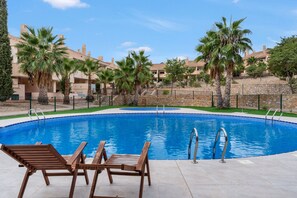 Piscina con sillones de descanso, rodeada de palmeras y un muro de piedra.