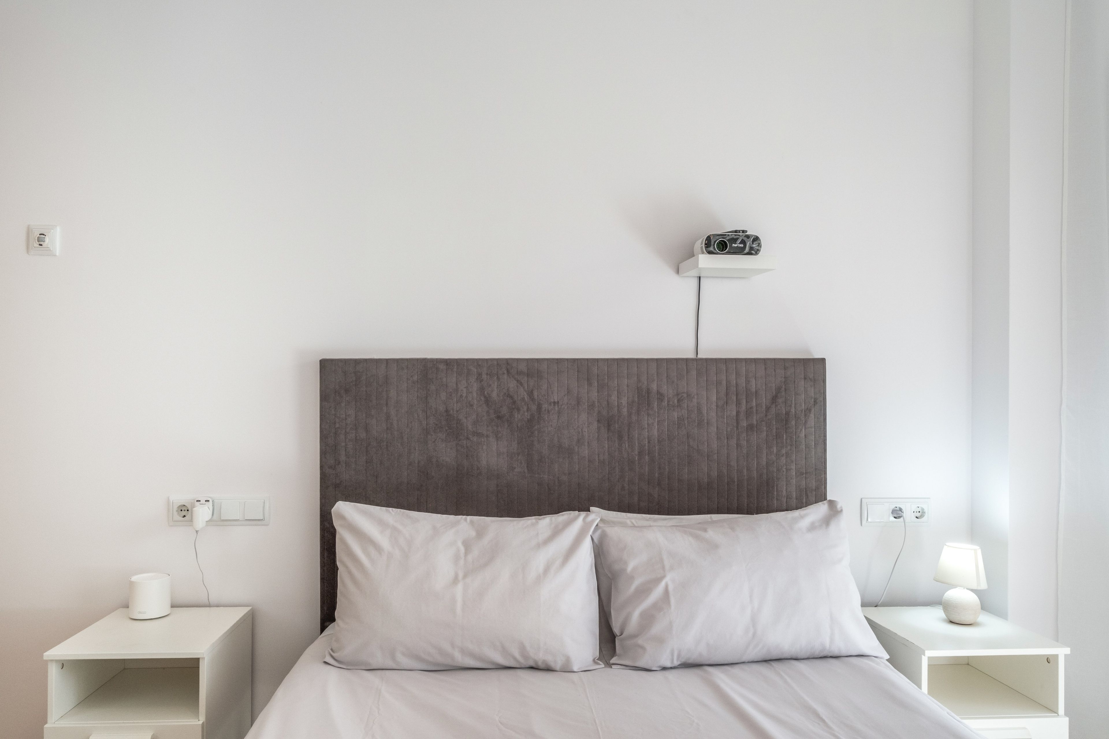 A minimalist hotel room with a large bed, two bedside tables, and a wall-mounted projector.