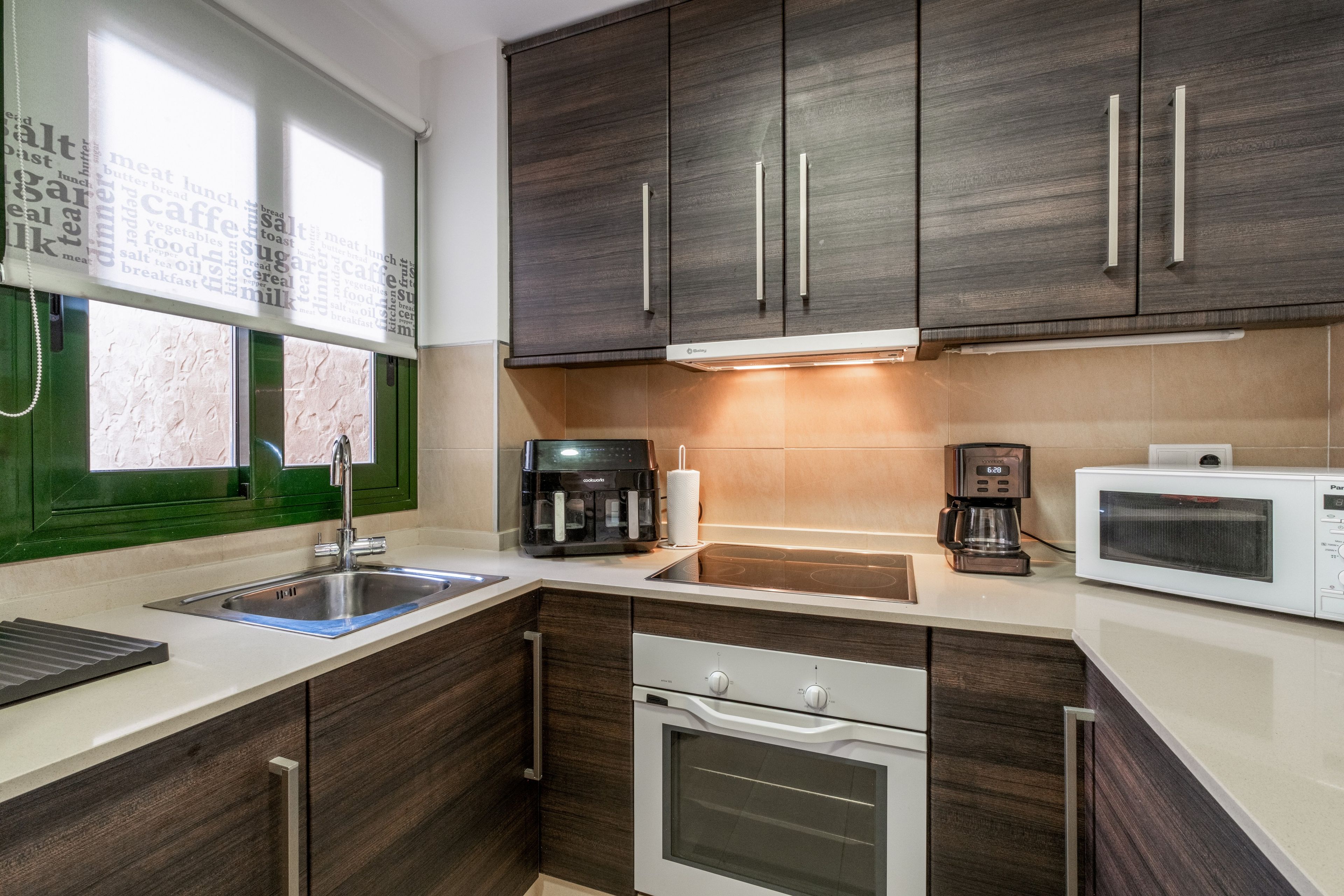 Een moderne keuken met donkere houten kasten, een roestvrijstalen spoelbak, een koffiezetapparaat, een magnetron en een oven.