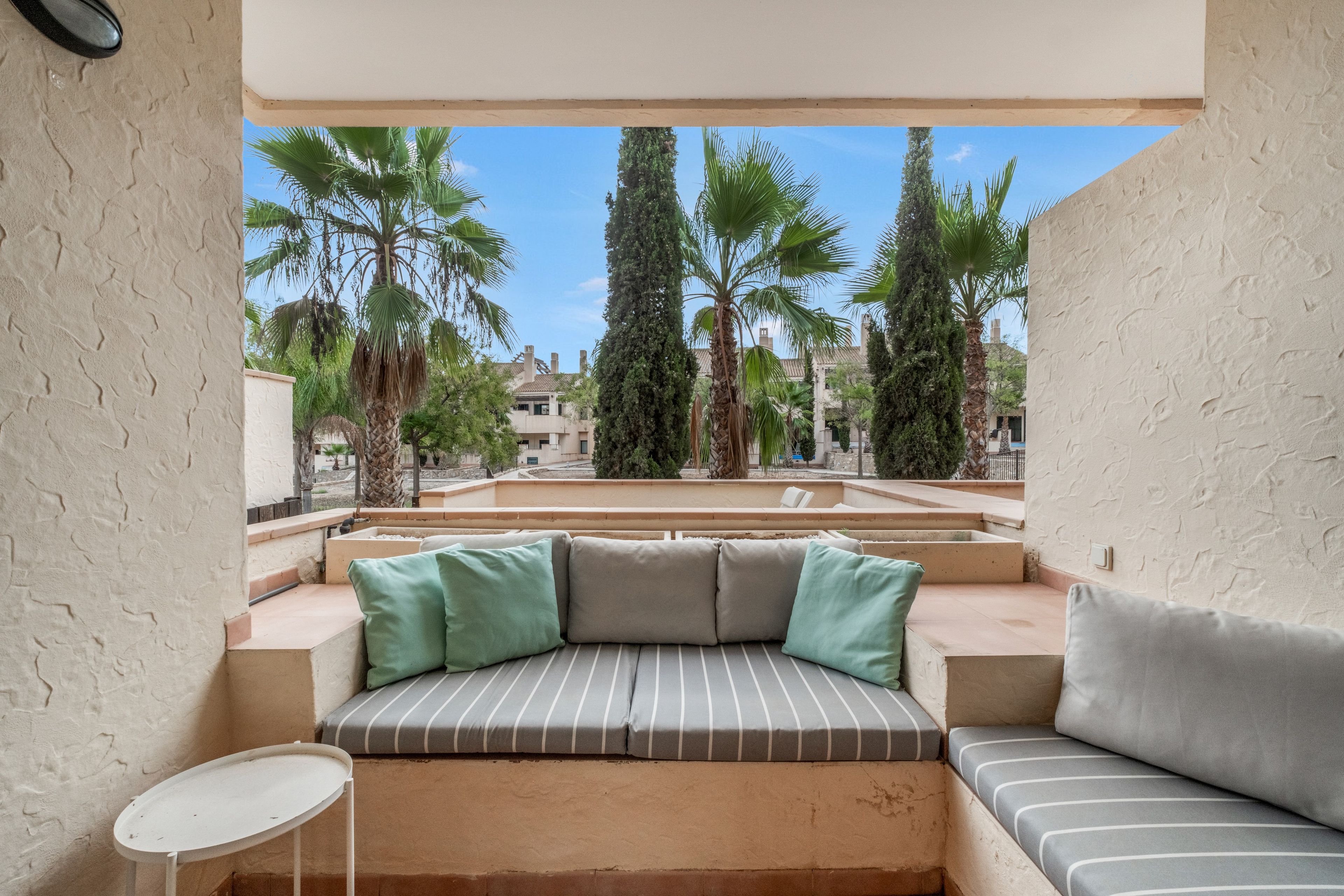 Un balcone con un'area salotto imbottita, un tavolino e vista su palme e edifici.