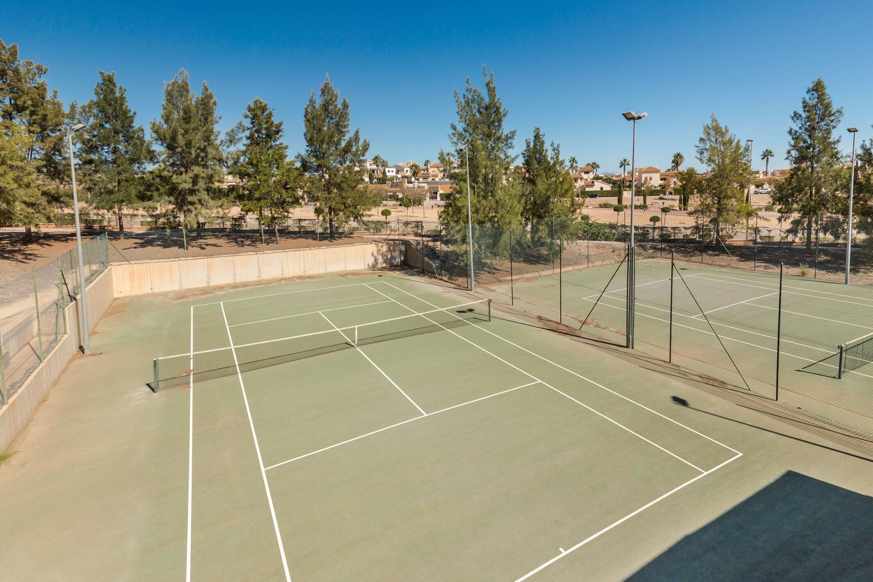 A tennis court with a net, surrounded by trees and a clear sky.