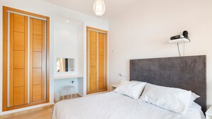 Ein Schlafzimmer mit einem Bett, einem Holzschrank und einem kleinen weißen Hocker.