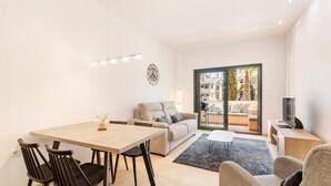 Ein modernes Wohnzimmer mit einer Couch, einem Esstisch mit Stühlen, einem Fernseher und einem großen Fenster mit Blick auf Gebäude.