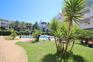 A hotel courtyard with a swimming pool, palm trees, and a clear blue sky. - MAENA Esmée - 🌴Appart` de Charme - Vue Marina, Clim & Piscine (Roses)