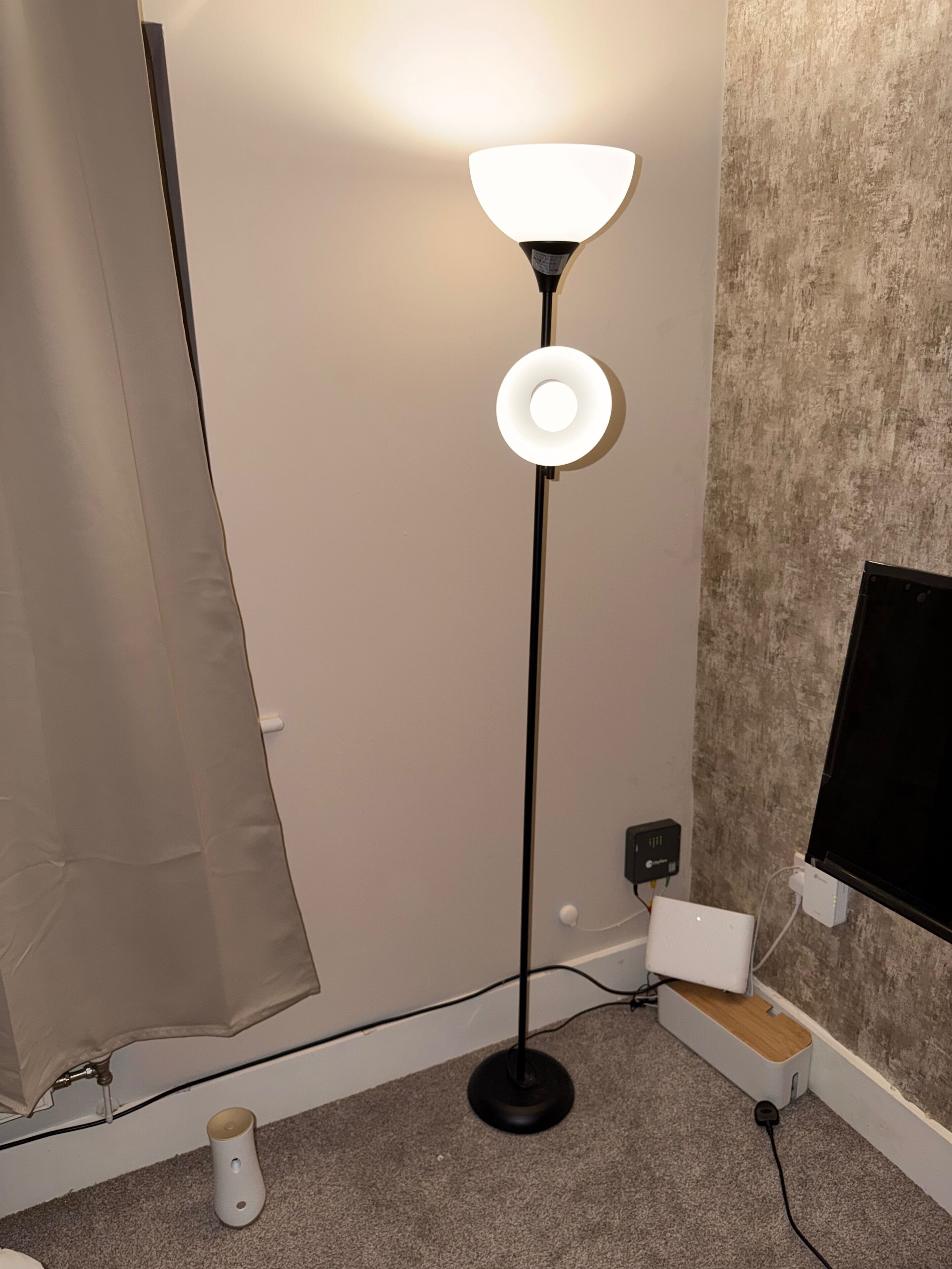 A room with a standing floor lamp, a television mounted on the wall, and a power outlet.