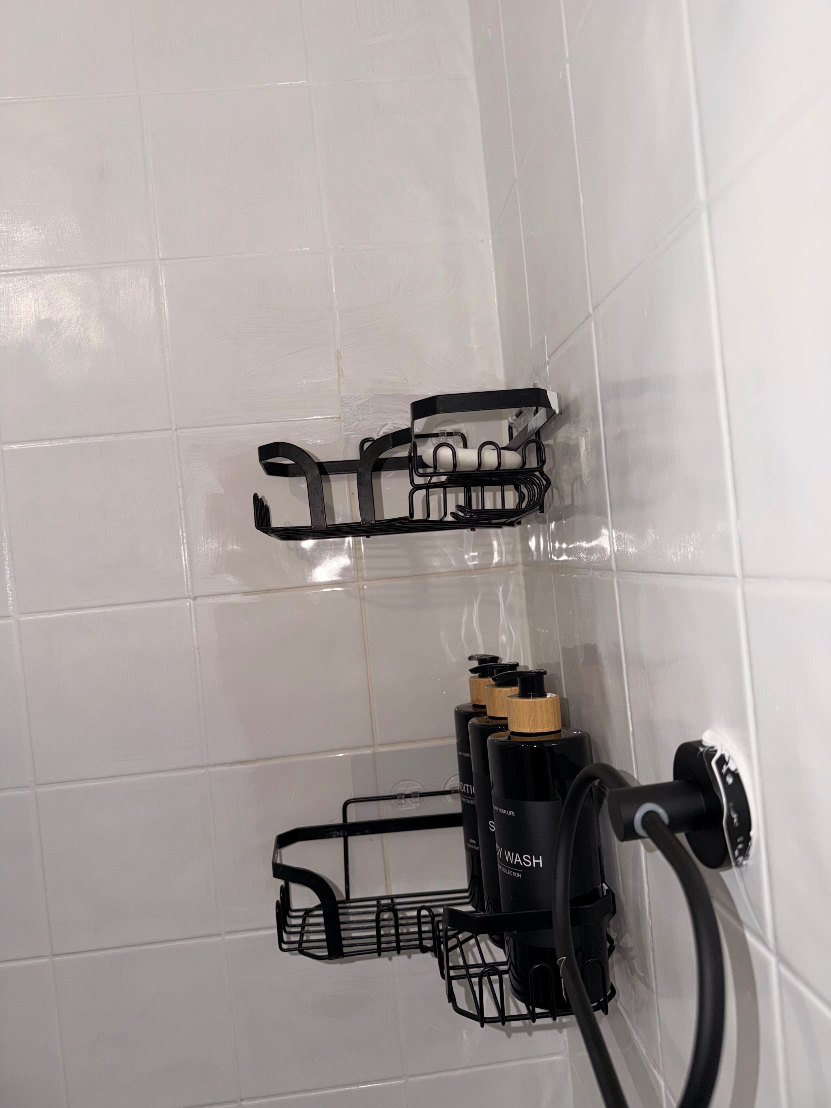 Een badkamer met witte betegelde wanden, een zwarte handdoekhouder en een zwarte zeepdispenser.