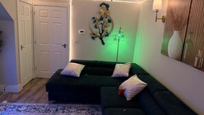 A modern living room with a dark green sofa, a patterned rug, and a decorative wall piece. - 2 Bedroom With Electric Charging and Parking (Gillingham)