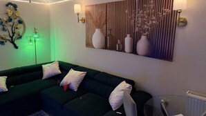 A modern living room with a dark green sofa, decorative wall art, and a floor lamp. - 2 Bedroom With Electric Charging and Parking (Gillingham)