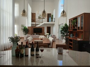 Ein geräumiger Wohnbereich mit Esstisch, Sofas und einer Kücheninsel, ausgestattet mit Weinflaschen und Gläsern.