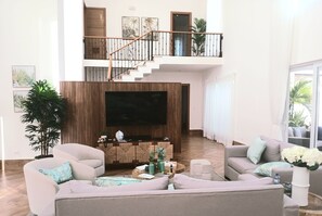 Ein großzügiger Wohnbereich mit einem großen Flachbildfernseher, zwei Sofas, einem Couchtisch und einer Treppe, die zu einer oberen Ebene führt.
