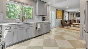 Une cuisine moderne avec des meubles gris, un plan de travail en marbre et une grande fenêtre.