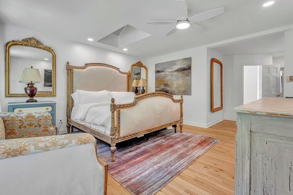 A bedroom with a bed, a ceiling fan, a mirror, and a painting on the wall.