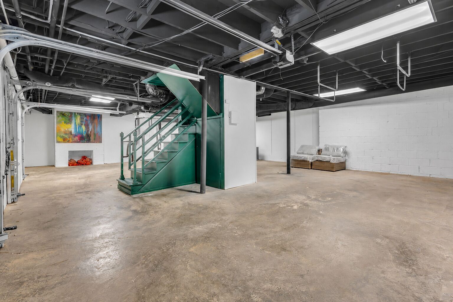 A spacious industrial-style room with a green spiral staircase, exposed ductwork, and a white brick wall.