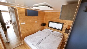 Une chambre de taille modeste, comprenant un lit, une petite table de chevet, un téléviseur fixé au mur et une fenêtre.