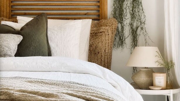 Una cama con cabecera de madera, una mesita de noche con lámpara y una planta colgante.