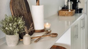 Una encimera de cocina con una tabla de cortar, un rollo de papel de cocina, una vela, una planta y utensilios de madera.