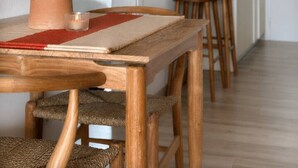 Una mesa de comedor de madera con un florero de trigo seco, un mantel individual rojo y sillas de mimbre.