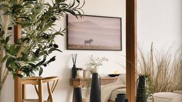 A room with a wooden floor, a wooden chair, a round wooden table with black vases, a wall-mounted picture of a horse, and a large plant.