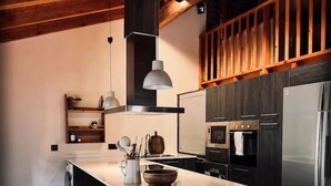 A modern kitchen with a large island, built-in appliances, and wooden ceiling beams. - Ático-Loft con encanto en el Centro de Camprodon (Camprodon)