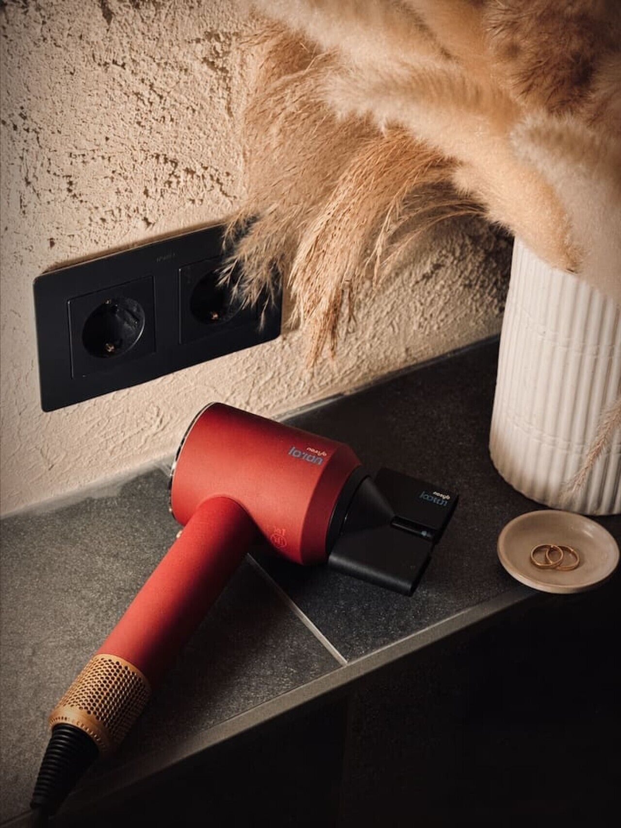 A red vacuum cleaner on a kitchen counter with a white vase and a pair of gold rings on a plate.