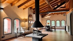 A spacious room with wooden beams, a fireplace, arched windows, and a dining area. - Ático-Loft con encanto en el Centro de Camprodon (Camprodon)