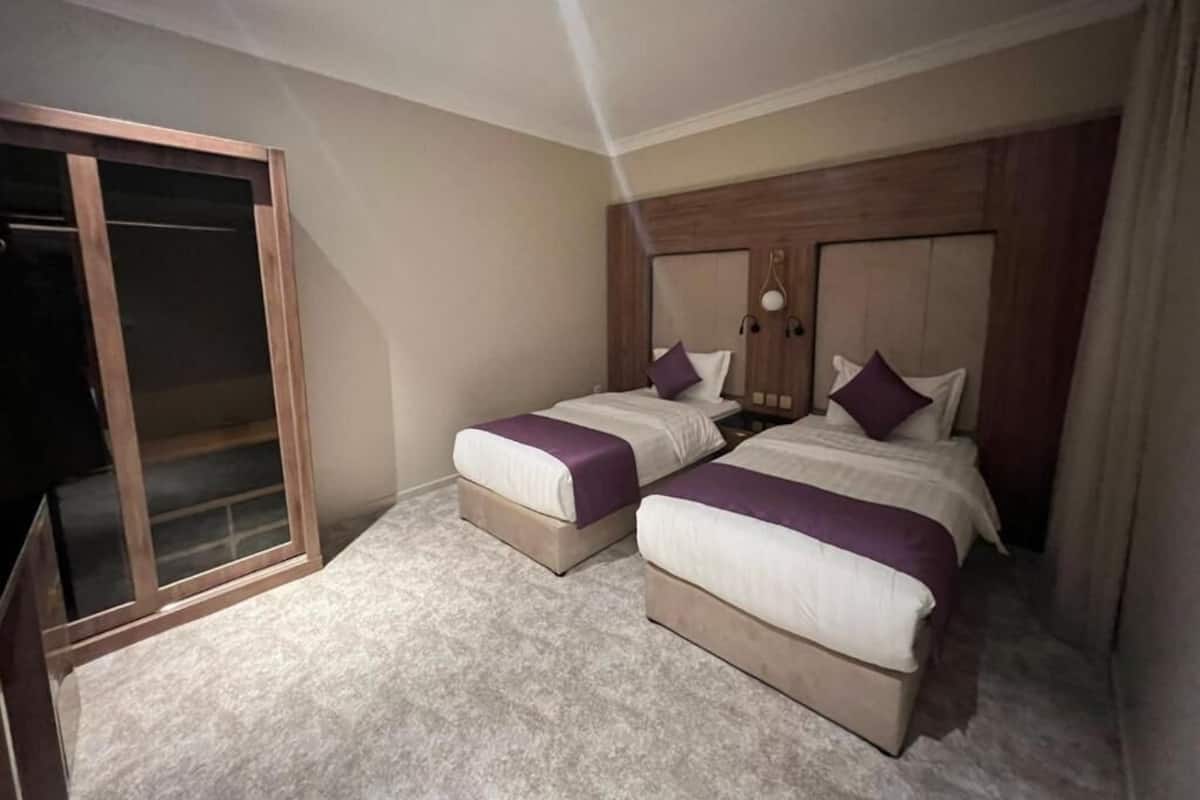 Quarto de hotel com duas camas, cabeceira de madeira, porta de correr de vidro e piso coberto de carpete.