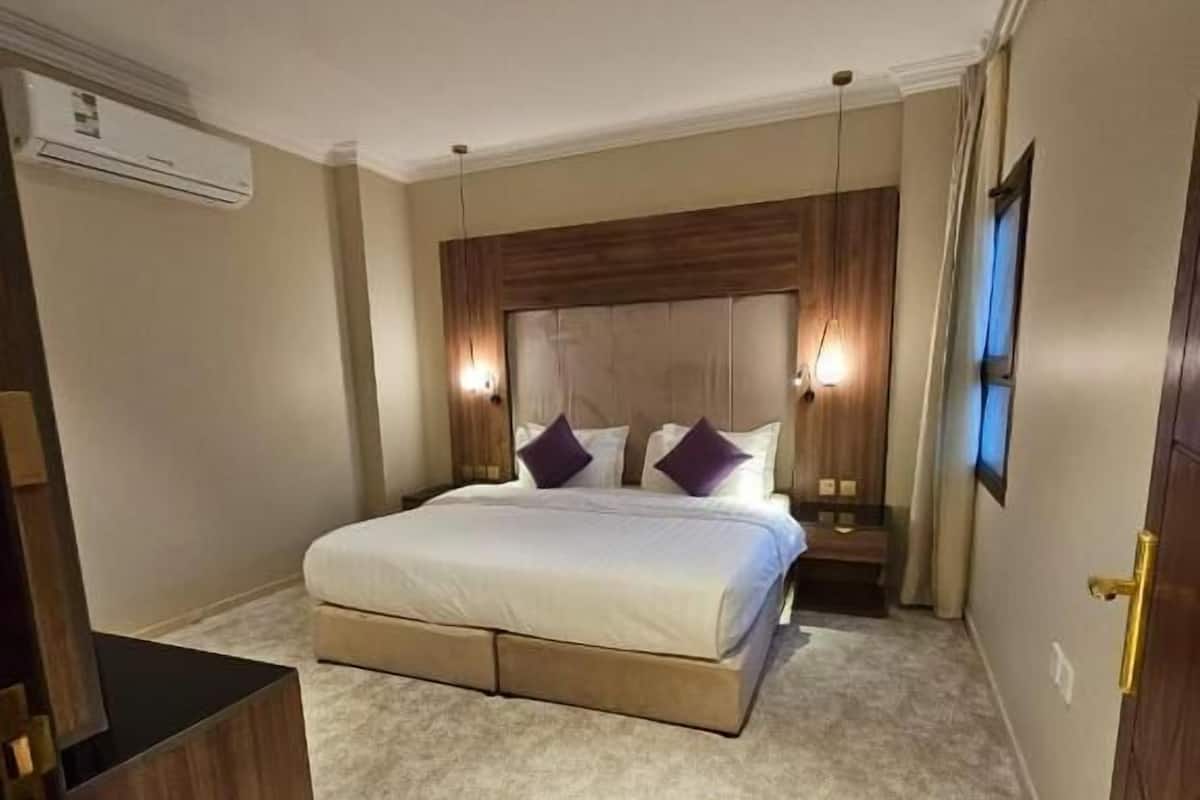 Quarto de hotel com cama, mesas de cabeceira, aparelho de ar condicionado, televisão e porta.