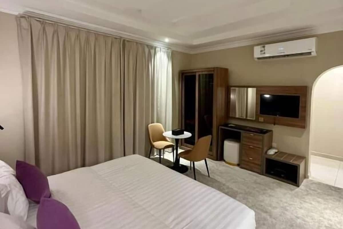 Quarto de hotel com uma cama grande, uma mesa, uma cadeira, uma televisão e um ar condicionado.