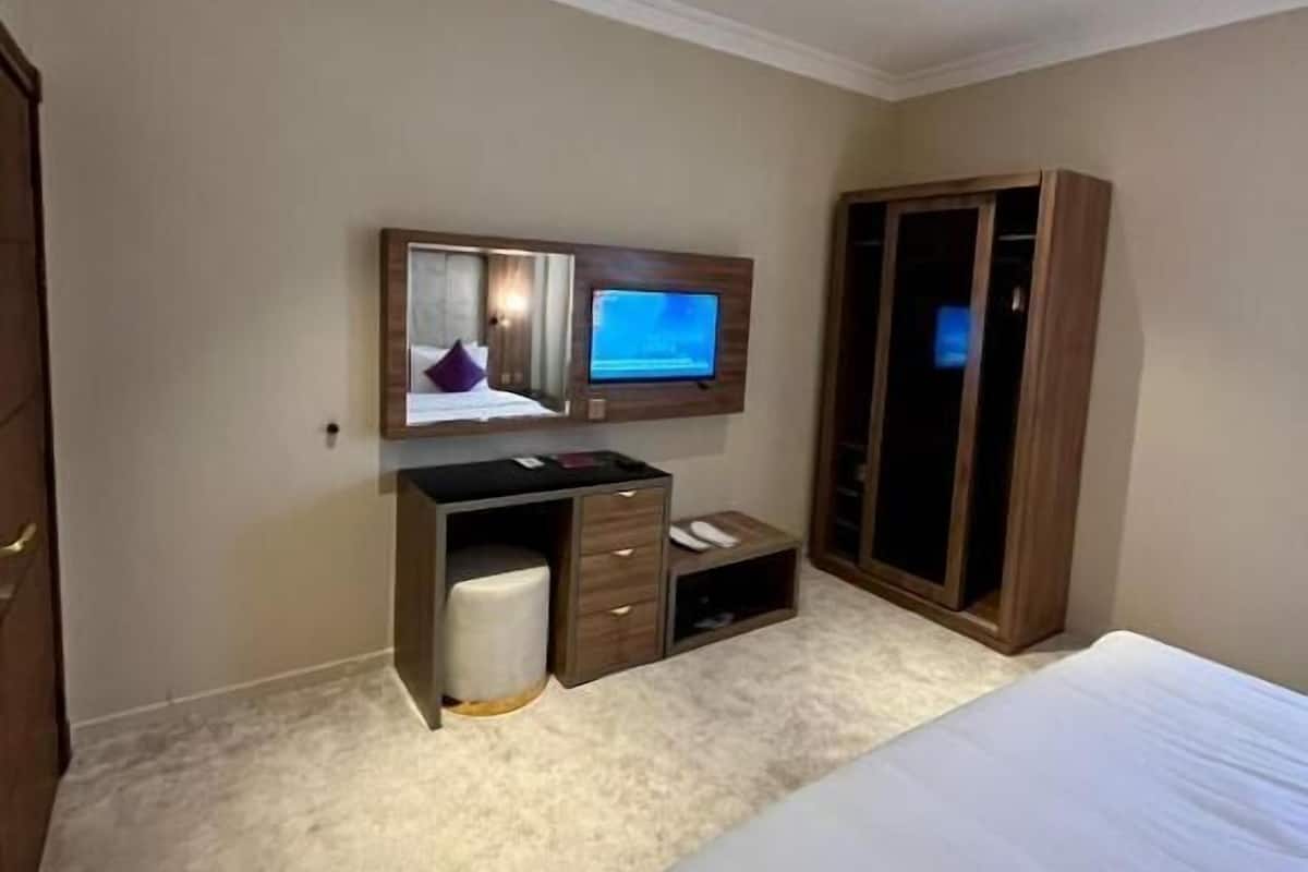 Um quarto com cama, escrivaninha com cadeira, guarda-roupa e televisão na parede.