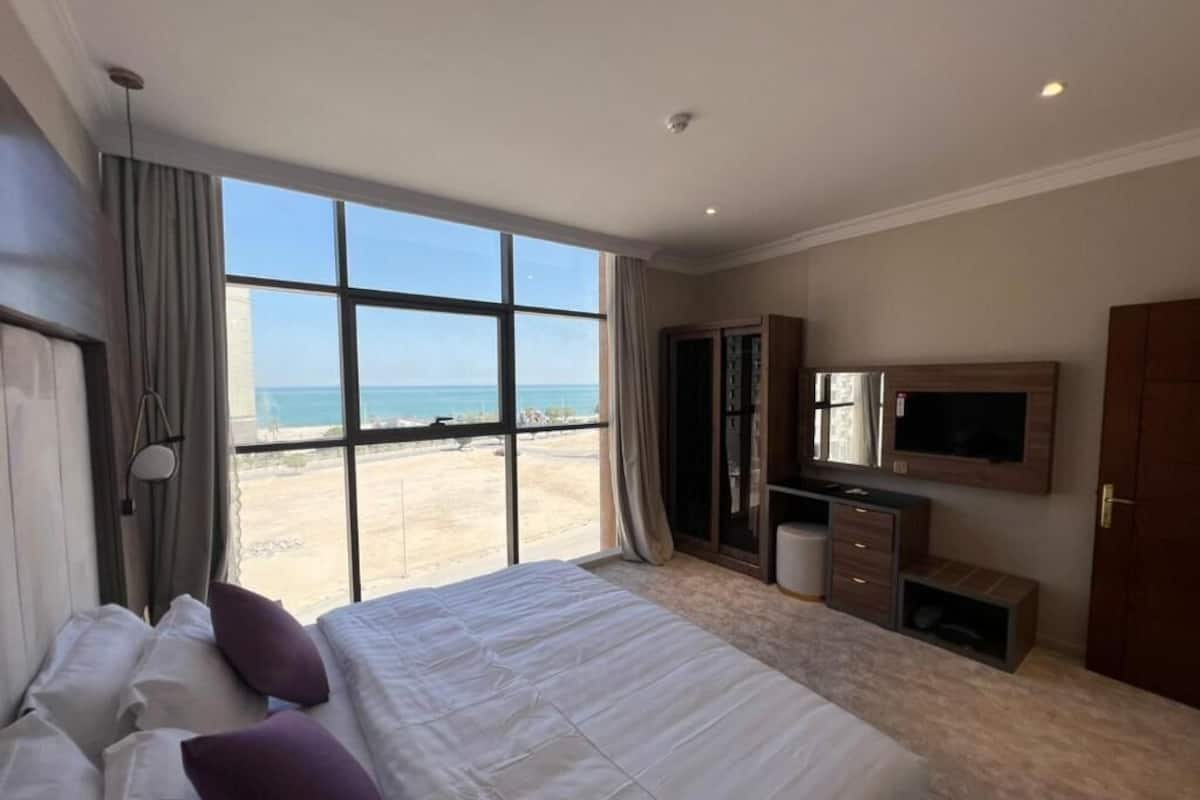 Quarto de hotel com uma cama grande, televisão, armário e vista para a praia.