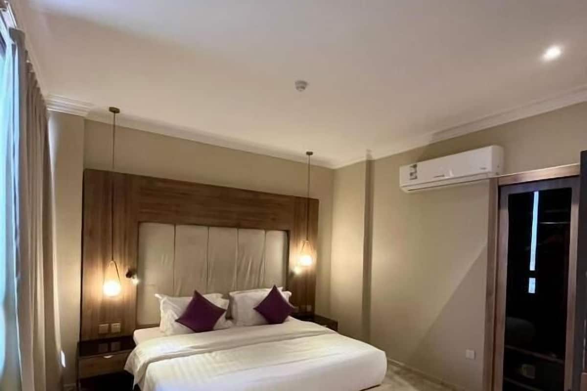 Quarto com cama, mesas de cabeceira, televisão e ar condicionado.