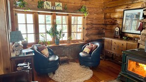 A cozy cabin interior with wooden walls, a stone fireplace, leather chairs, a wooden desk, and a window with a view of greenery. - Cozy 1-bedroom log cabin in beautiful Manitowish Waters/Winchester (Manitowish Waters)