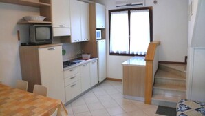 A compact kitchen with white cabinets, a small dining table, and a window with curtains. - Townhouse With Enclosed Private Garden (San Michele al Tagliamento)