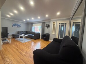 Ein modernes Wohnzimmer mit einer Couch, einem Couchtisch, einem Fernseher und einem großen Fenster.
