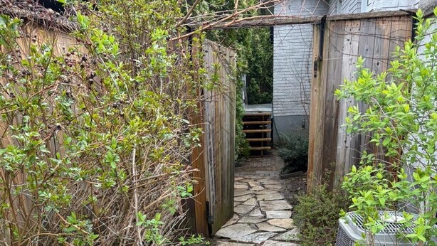 Un chemin de pierres menant à une porte en bois, entouré de verdure et bordé d’une petite construction.