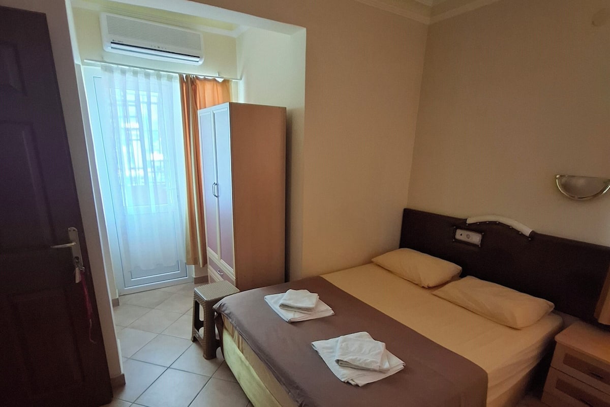 A hotel room with a bed, a nightstand, a wardrobe, a mirror, and a ceiling light fixture.