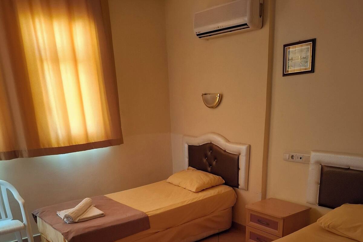 A hotel room with two beds, a chair, a small table, and an air conditioning unit on the wall.