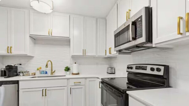 A modern kitchen with white cabinetry, gold handles, a built-in microwave, and a stove.