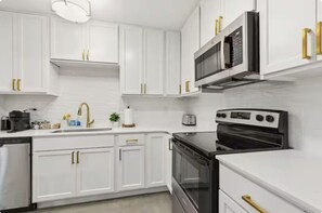 Una cocina moderna con armarios blancos, tiradores dorados, microondas integrado y estufa.