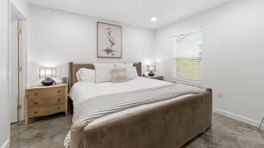 A bedroom with a bed, bedside tables, a wall-mounted artwork, a window with blinds, and a door.