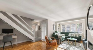 A living room with a staircase, a green sofa, a wooden coffee table, and a television.