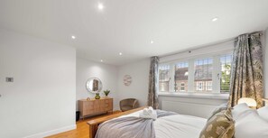 A bedroom with a bed, a wooden bench, a dresser, a chair, a window with curtains, and a radiator.