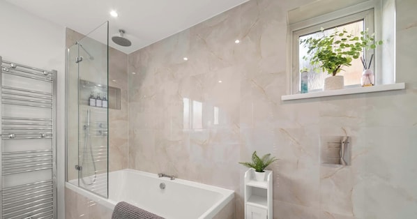Un baño moderno con ducha envuelta en vidrio, una bañera blanca y un estante con una planta en maceta.