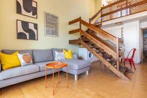 A living room with a grey sofa, a wooden staircase, and a washing machine in the background. - Apartment Luna, modern, 100 m from the sea (L'Escala)
