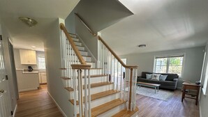 A staircase with wooden steps and white railings, leading to a living area with a sofa and a window. - Spacious 4 bedroom PRIVATE HOME
centrally located to all the Cape has to offer (Barnstable)